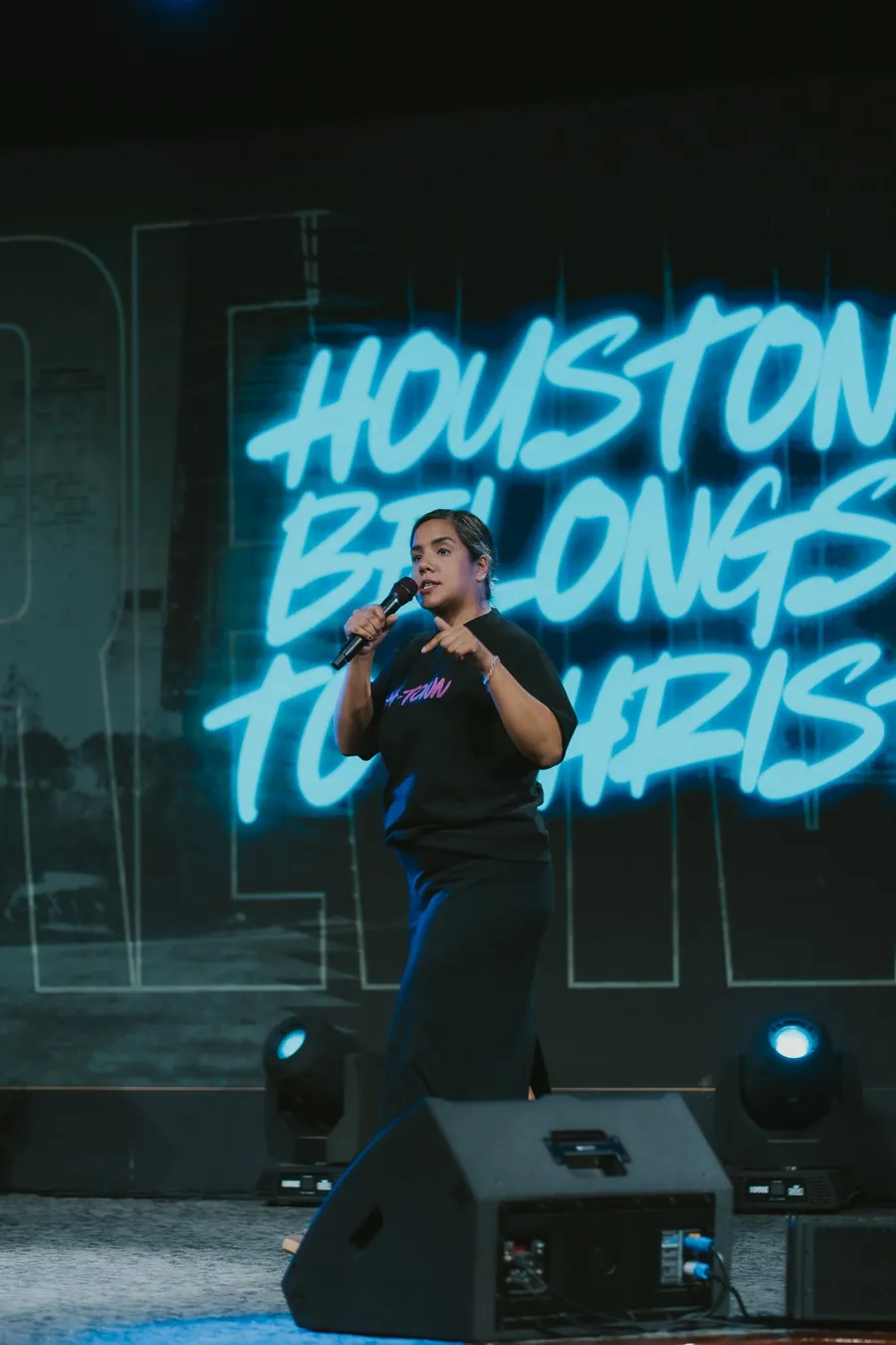 Mujer cantando en el escenario junto al letrero de neón «Houston Belongs to Christ»