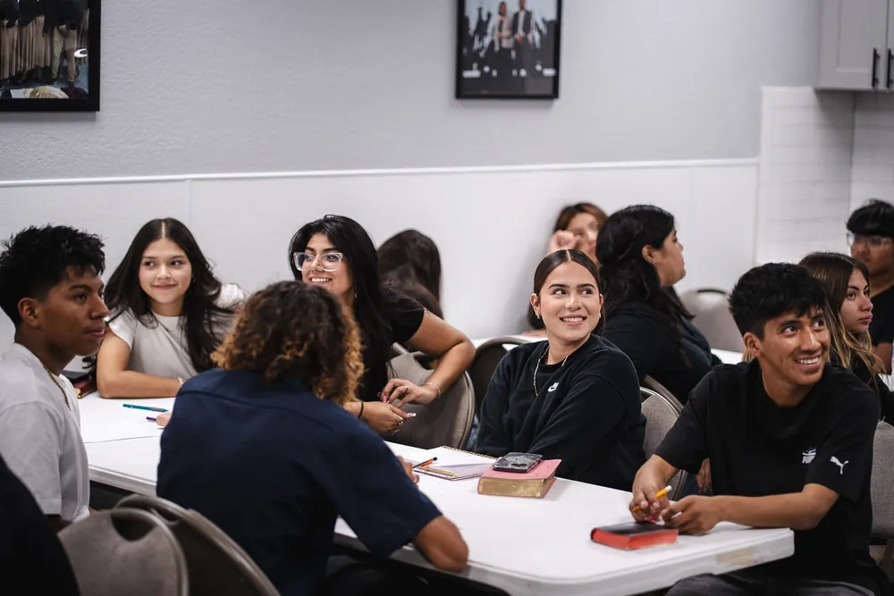 Jóvenes de la iglesia reunidos alrededor de una mesa, sonriendo y conversando